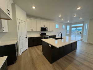 Kitchen featuring dark cabinetry, a kitchen island with sink, white cabinetry, light wood-style flooring, and recessed lighting