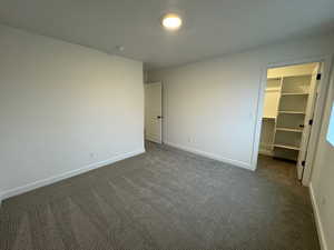 Unfurnished bedroom with a walk in closet and dark carpet