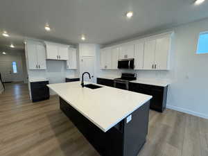 Kitchen with dark cabinets, white cabinets, a kitchen island with sink, recessed lighting, and appliances with stainless steel finishes