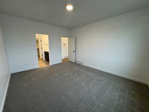 Unfurnished bedroom featuring dark colored carpet and connected bathroom