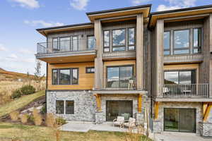 Rear view of house featuring a balcony, a patio area, stone siding, and a yard
