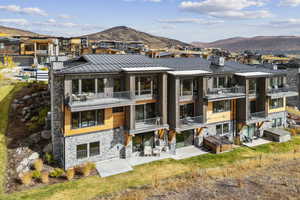 Back of house featuring a standing seam roof, stone siding, a metal roof, a patio area, and a balcony