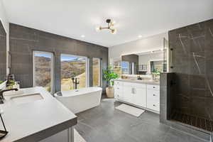 Bathroom featuring two vanities, tile walls, walk in shower, a freestanding tub, and plenty of natural light
