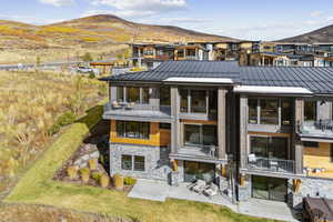 Rear view of property featuring a balcony, a standing seam roof, a patio area, a mountain view, and stone siding