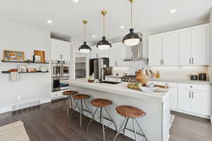 Kitchen with white cabinets, a breakfast bar, tasteful backsplash, dark wood-style floors, and an island with sink