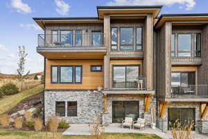 Back of property featuring a balcony, stone siding, a patio, and a lawn