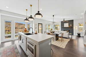 Kitchen with a fireplace, light countertops, open floor plan, stainless steel microwave, and an island with sink