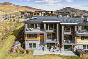 Back of property with a balcony, a patio area, stone siding, a standing seam roof, and a mountain view