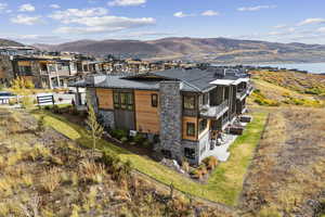 Back of house with stone siding, a metal roof, a mountain view, and a lawn