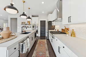 Kitchen featuring white cabinetry, dark wood finished floors, appliances with stainless steel finishes, wall chimney exhaust hood, and decorative backsplash