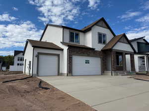 View of front of home featuring stucco siding, driveway, brick siding, covered porch, and an attached garage