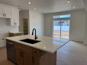 Kitchen with recessed lighting, dishwasher, brown cabinetry, a textured ceiling, and a kitchen island with sink