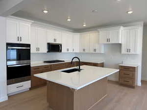 Kitchen with white cabinets, appliances with stainless steel finishes, brown cabinets, light wood finished floors, and an island with sink
