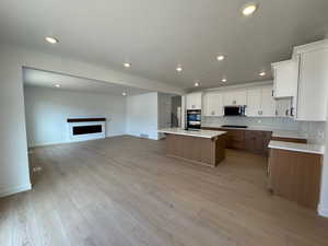 Kitchen featuring brown cabinets, white cabinets, open floor plan, a textured ceiling, and light wood-style flooring