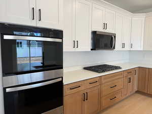 Kitchen with stainless steel appliances, light wood-style floors, white cabinetry, and light stone countertops