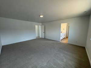 Unfurnished bedroom with a textured ceiling, light colored carpet, and ensuite bath