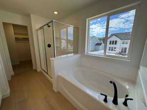 Bathroom featuring a stall shower, a garden tub, a spacious closet, light wood-type flooring, and recessed lighting
