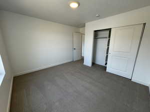 Unfurnished bedroom featuring dark colored carpet, a closet, and a textured ceiling
