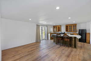 Kitchen featuring glass insert cabinets, freestanding refrigerator, a breakfast bar area, light wood-style floors, and recessed lighting