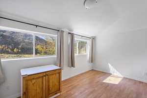 Unfurnished bedroom with lofted ceiling, light wood finished floors, and a mountain view