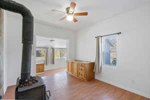 Living room with a wood stove, light wood-type flooring, and ceiling fan