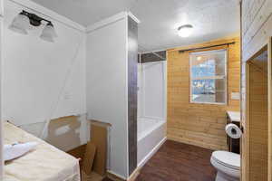 Full bathroom with wood walls, vanity, dark wood-style floors, a textured ceiling, and shower / bath combination