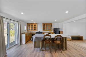 Kitchen with a center island, glass insert cabinets, a breakfast bar, light wood-style floors, and brown cabinetry