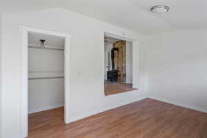 Unfurnished bedroom with a wood stove, wood finished floors, vaulted ceiling, and a spacious closet