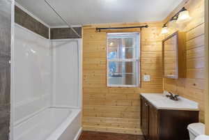 Bathroom with wood walls, shower / bath combination, vanity, dark wood-style flooring, and a textured ceiling