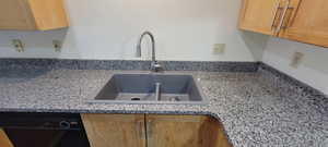 Kitchen view of black dishwasher, light stone countertops, brown cabinetry, and light brown cabinetry