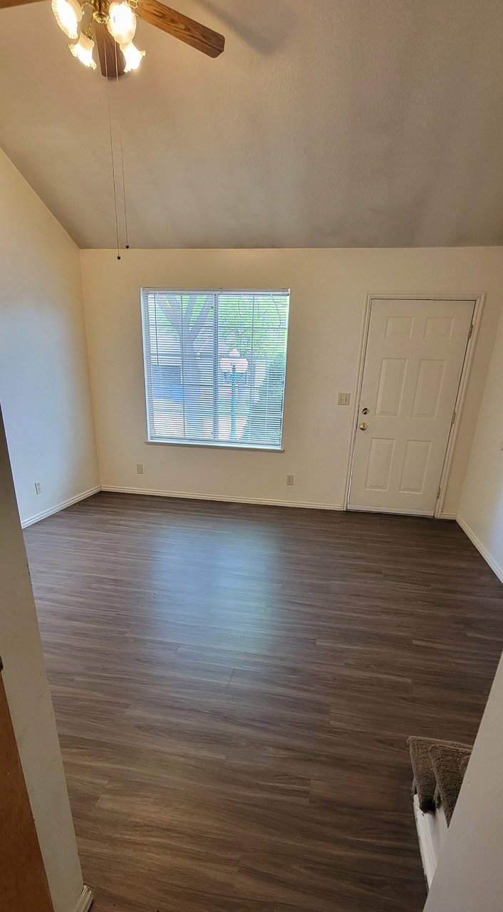 Unfurnished living room featuring dark wood-type flooring, lofted ceiling, and a ceiling fan