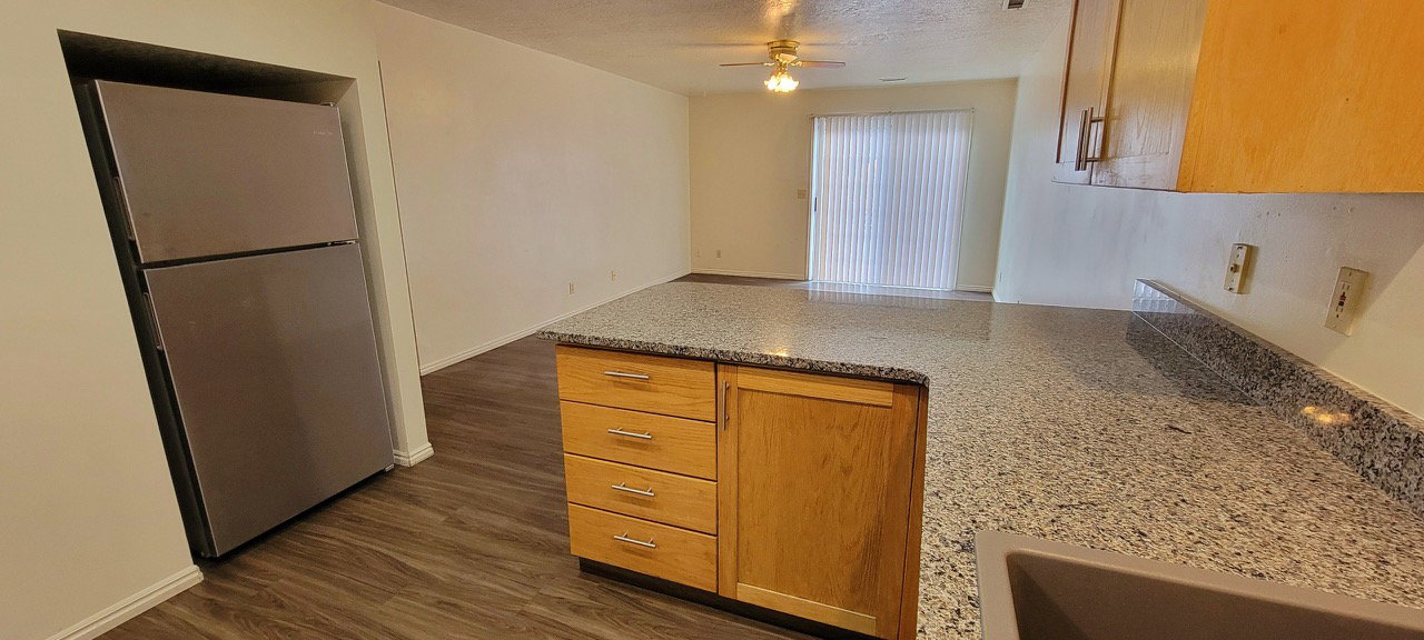 Kitchen with a peninsula, freestanding refrigerator, light stone counters, dark wood-type flooring, and a textured ceiling