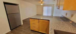 Kitchen with a peninsula, freestanding refrigerator, light stone counters, dark wood-type flooring, and a textured ceiling