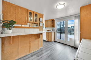 Kitchen featuring tile counters, glass insert cabinets, dark wood finished floors, a textured ceiling, and backsplash