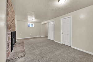 Below grade area with light carpet, a stone fireplace, and a textured ceiling