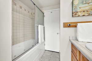 Bathroom featuring a combined bath / shower with jetted tub, light tile patterned floors, and vanity