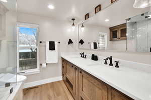 Full bath with light wood-type flooring, double vanity, a marble finish shower, and recessed lighting