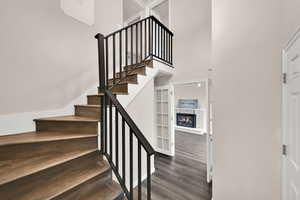 Stairway featuring a brick fireplace, wood finished floors, and a towering ceiling