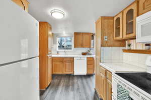 Kitchen featuring white appliances, a textured ceiling, decorative backsplash, dark wood-type flooring, and glass insert cabinets