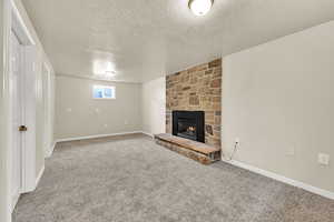Unfurnished living room featuring a textured ceiling, carpet flooring, and a stone fireplace
