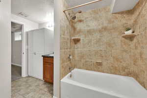 Bathroom with bathing tub / shower combination, light tile patterned floors, a textured ceiling, and vanity