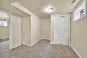 Unfurnished bedroom featuring a textured ceiling, light carpet, and a closet