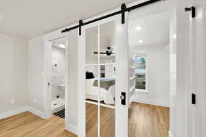 Unfurnished bedroom with light wood-type flooring, ensuite bathroom, a barn door, and recessed lighting