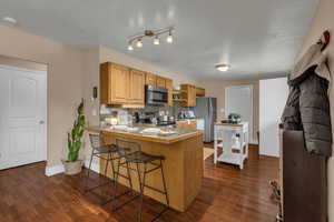 Kitchen featuring backsplash, dark wood-style floors, a kitchen bar, stainless steel appliances, and a peninsula