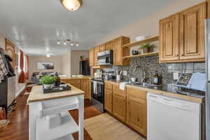 Kitchen featuring open shelves, stainless steel appliances, decorative backsplash, a peninsula, and dark wood finished floors