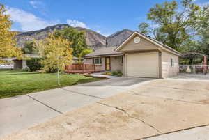 Single story home with driveway, brick siding, an attached garage, and a deck with mountain view