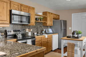 Kitchen with stainless steel appliances, tasteful backsplash, open shelves, light wood-type flooring, and brown cabinetry