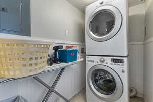 Laundry area featuring electric panel, a wainscoted wall, and stacked washer / drying machine
