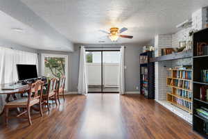 Home office with a textured ceiling, dark wood-type flooring, and ceiling fan