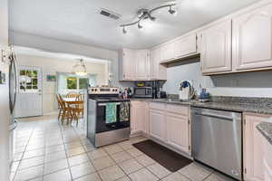 Kitchen with appliances with stainless steel finishes, light tile patterned flooring, dark stone counters, white cabinetry, and a textured ceiling